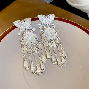 Detailed macro view of silver hollow butterfly tassel earrings on a ceramic dish