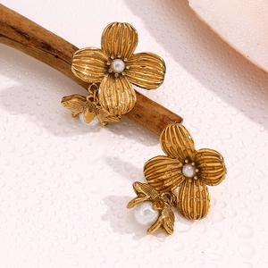 Macro shot of gold floral earrings with pearls on a branch with water droplets