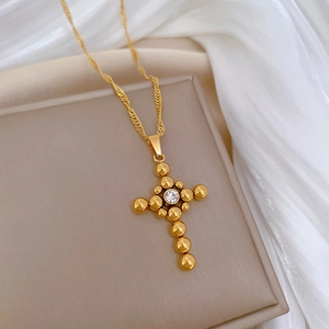 Gold titanium steel beaded cross necklace with zircon center on beige display tray
