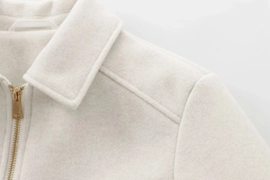 Detailaufnahme einer cremefarbenen Tweedjacke mit Goldreißverschluss und Reversnähten