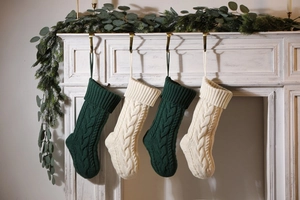 Deep green and off-white knitted Christmas stockings hanging on a white fireplace