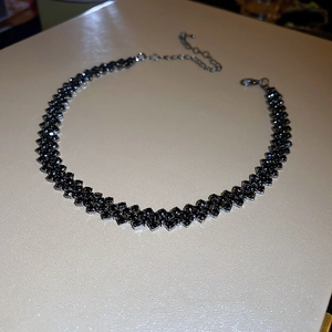 Close-up of black beaded choker necklace with geometric diamond texture and metal clasp