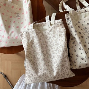 Detailed view of three cotton tote bags with floral prints on a wooden stool