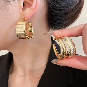 Detail of wide C-shaped gold hoop earrings with horizontal stripes and metallic texture