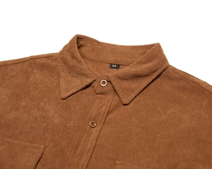 Dettaglio della texture in velluto a coste marrone e bottoni ambra sulla camicia