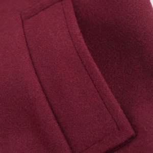 Detail shot of the pocket stitching and soft wool fabric texture on a wine red coat