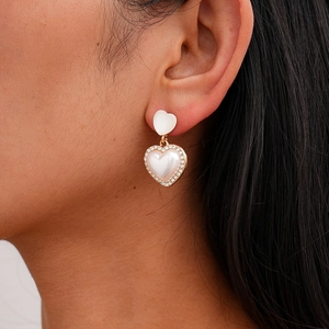 Close-up of golden heart earrings with pearls and crystals worn on a model's ear