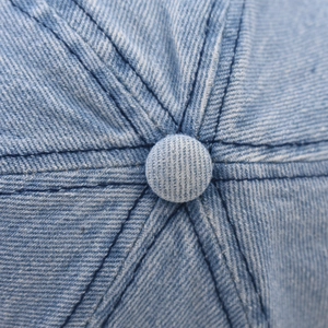 Gros plan du bouton supérieur et des coutures d'une casquette en jean bleu délavé