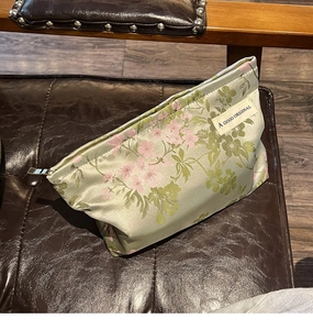 Detail of silk-texture floral makeup bag with pink flowers on a premium green fabric