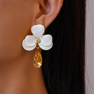 Détail de boucles d'oreilles fleurs avec pétales blancs, cœur doré et goutte jaune gemme