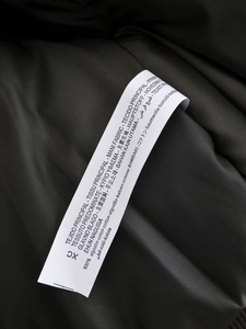 Close-up detail of the 100% cotton material fabric label on a green bomber jacket
