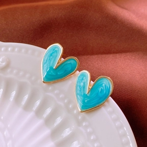 Macro shot of blue marble pattern heart stud earrings with golden edges on ceramic dish