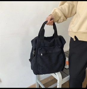 Detail of black canvas backpack showing front zipper pocket and durable buckle hardware