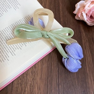 Detailed view of cream resin hair claw with green satin bow and purple fabric tulips