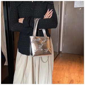Detail of silver handbag with metallic bow accents and a chain strap shown by a model