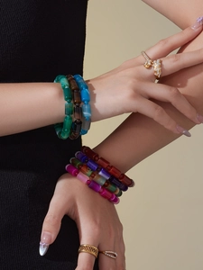 Detail gestapelter Boho-Natursteinarmbänder und funkelnder goldener Blumenringe am Handgelenk