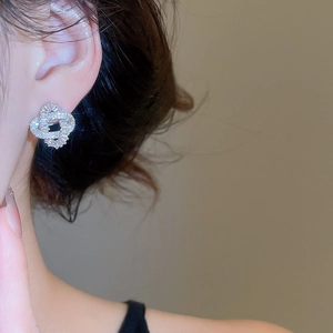 Close-up of geometric intertwined zircon stud earrings worn on female ear