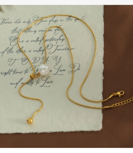 Detailaufnahme der goldenen Y-Halskette mit weißen Perlen und Karabinerverschluss auf Papier