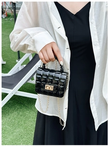 Detail of black quilted jelly bag with gold buckle and chain strap on green grass