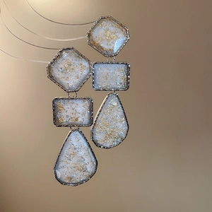 Macro detail of geometric resin earrings with gold and silver foils in warm tones