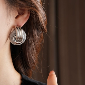 Close-up of a silver-tone round hollow mesh stud earring worn by a model