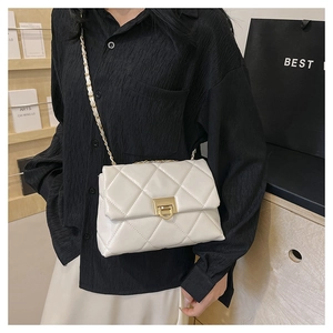Quilted beige crossbody bag with gold chain strap shown on a model in a modern interior