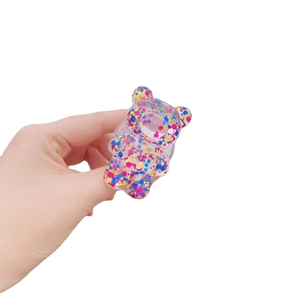 Handheld view of a transparent bear-shaped phone grip with vibrant colorful glitter inside