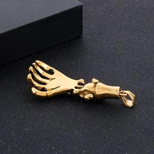 Macro shot of gold-plated skeleton hand pendant on a textured black background
