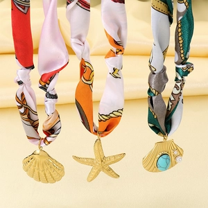 Détail macro de pendentifs étoile de mer et coquillage avec turquoise sur foulard de soie