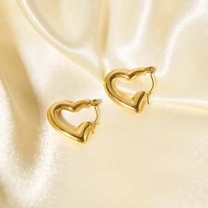 Dettaglio macro di orecchini a cuore in acciaio inossidabile oro 18K su seta champagne