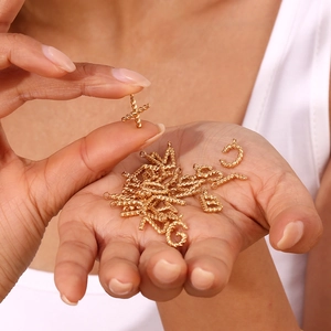 Detailed macro view of small 18K gold-plated twisted rope initial charms held by hand