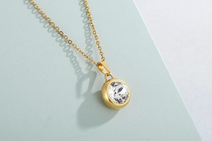 Detailed close-up of golden necklace featuring a sparkling round crystal pendant on soft green surface
