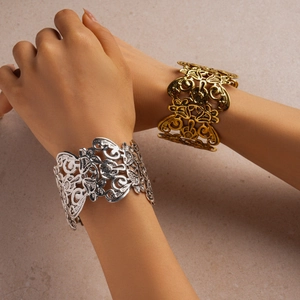 Close-up of gold and silver hollowed-out floral cuffs on stone surface texture
