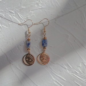 Detail of gold earrings featuring blue marbled beads and celestial eye moon pendants