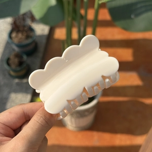 Elegant cream white wavy hair claw clip held in hand with natural sunlight shadows