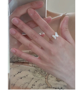 Close-up of a delicate gold ring featuring a white butterfly design worn on a finger