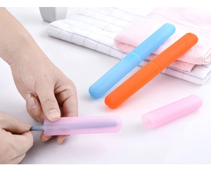 Hand holding colorful portable travel toothbrush cases in blue, orange, and pink