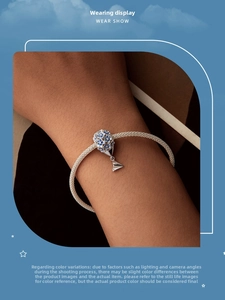 Detailed view of silver braided bracelet with blue enamel flower bead and paper plane charm