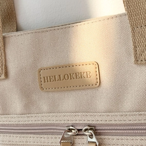 Detail of beige canvas tote bag showing the leather logo patch and interior zip pocket