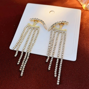 Macro detail of gold tassel earrings featuring dense rhinestones and a semi-circular arc design