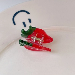 Detailed view of mini strawberry hair claw clip made of red acetate on a white plate