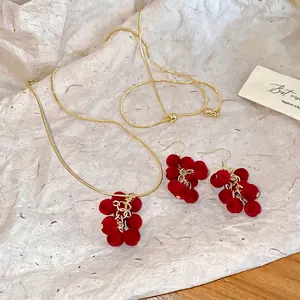 Elegant gold necklace and earring set with red velvet grape tassels on off-white paper