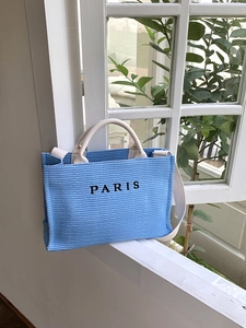 Detailed texture of blue woven tote bag featuring black Paris embroidery on front
