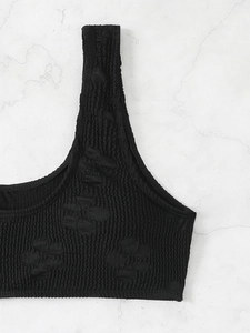 Black smocked bikini top with 3D floral texture on a minimalist marble backdrop