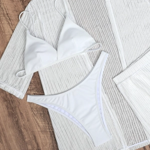 Detailed flat lay of white three-piece bikini set with sheer mesh knit cover-up on wood