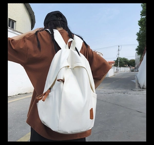 Minimalist white canvas backpack on model featuring brown leather zipper and label accents