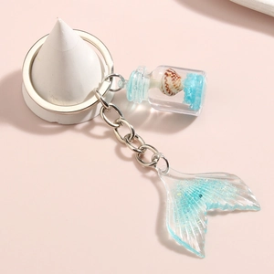 Close-up of glittery resin mermaid tail charm and glass shell bottle on ocean keychain