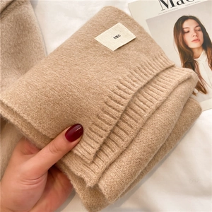 Detailed view of beige ribbed knit texture and woven emo brand label on a soft scarf