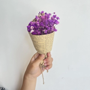Close-up of a mini dried purple gypsophila bouquet wrapped in vintage newspaper style paper
