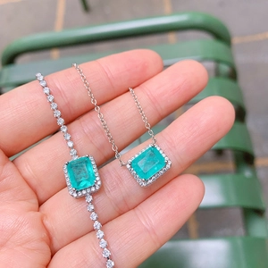 Detail showing hand-held silver necklace and bracelet set with green rectangle gemstones